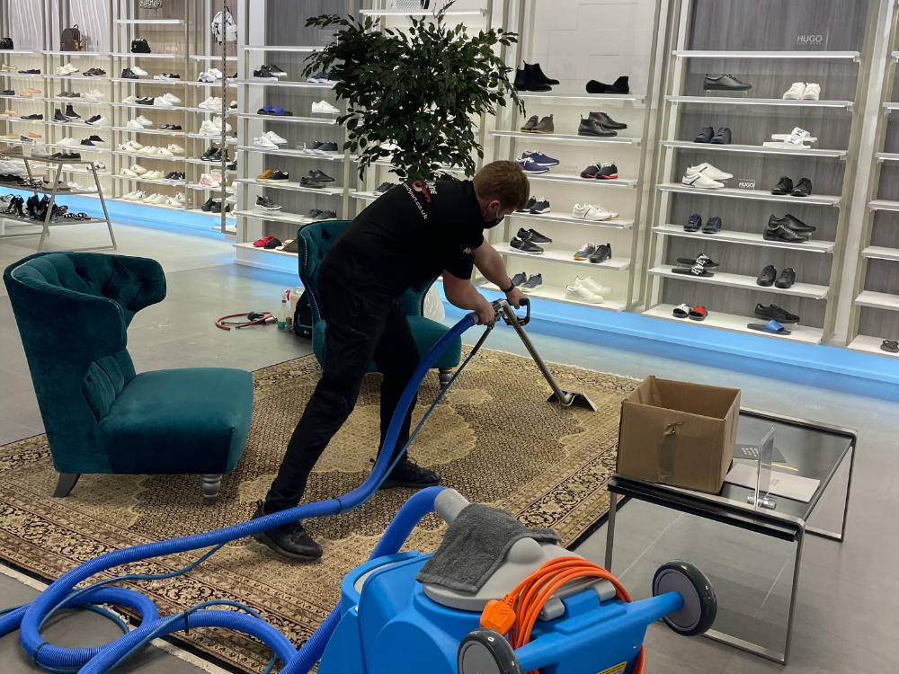 A Rise & Shine Cleaning worker cleaning a rug inside a large clothing store